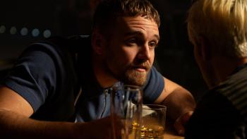 Three Day Millionaire: A young White man in a bar leans forward to talk intently to a friend