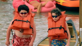 Tiny Fugitives movie: Two 12-year-old boys walk on a lake deck wearing sunglasses and giant life jackets