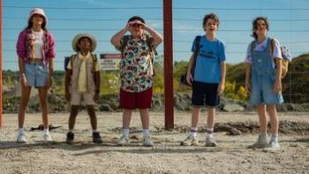 Tiny Fugitives movie: Five 12-year-olds stand in front of a fence, the boy in the center looking through binoculars