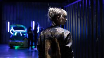 Titane: Blonde woman in leather jacket seen from behind with room lit in blue before her