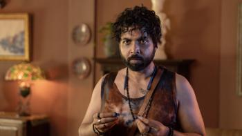 Toaster: An Indian man with curly hair and tank top holding some ear buds, standing in a warmly lit room