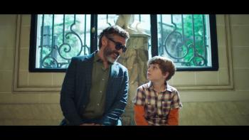 A man and boy sitting in front a window smile and talk.