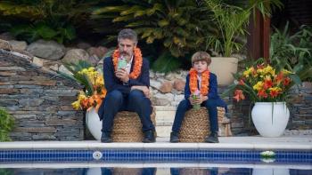 A man and boy wearing leis sit dejectedly in front of a swimming pool.