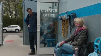 Tow movie: Simon Rex pokes his head outside the dispatch office of a tow company to talk to Rose Byrne, who's sitting on a bench outside