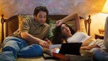 Transmitzvah: Two people lounge in a bed with a laptop
