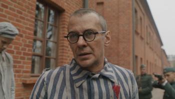 Triumph of the Heart movie: Marcin Kwaśny stands outside Auschwitz in a striped prison uniform