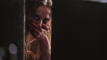 Trust movie: Sophie Turner is wet and in distress, sitting down in a dark area, covering her mouth