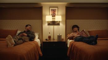 Twinless movie photo: Dylan O'Brien and James Sweeney lie on twin beds and talk in a hotel room