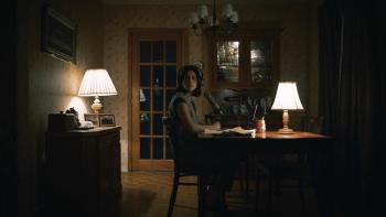 Undertone Movie: Seated at a kitchen table with her headphones and mic, Evy (Nina Kiri) looks as if she's heard something