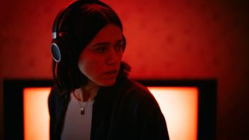 Undertone Movie: Against a red background, Evy looks worried while wearing her headphones