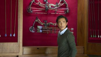 Untitled Home Invasion Romance: Justin H. Min in front of a weapons cache.