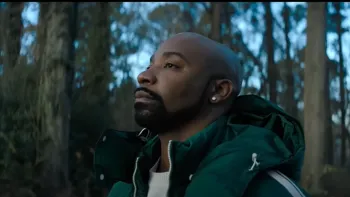Untold: Shooting Guards movie: Ex-NBA player Javaris Crittenton center wears green winter coat with hood with trees and woods behind him