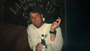 Untold: The Fall of Favre movie: Brett Favre in buttoned shirt center holds beer in one hand, black hat in other, in front of Lambeau Field sign