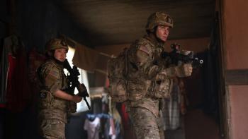 Valiant One movie: Chase Stokes stands in front of Lana Condor while aiming his gun