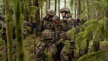 Valiant One movie: Two soldiers support a third as they walk through the jungle.