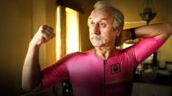 Vijay 69 movie: Older Indian man with white hair in pink tracksuit flexes his arm muscles while in his dining room