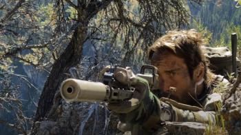 Warhorse One: Master Chief Richard Mirko shoots rifle next to rock wearing camouflage.