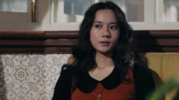 The Way of the Dragon movie: Nora Miao sits in restaurant with a window behind her and a plant in front of her.