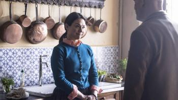 Mr. Blake at Your Service!: A younger White woman  stands in front of a kitchen sink, smiling at a bald, older White man