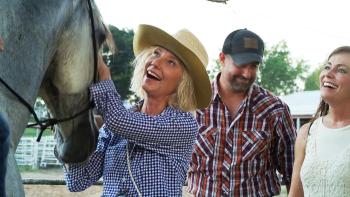 Wildfire: The Legend of the Cherokee Ghost Horse movie: Anne Heche laughs while she pats the nose of a horse; a woman and man smile behind her