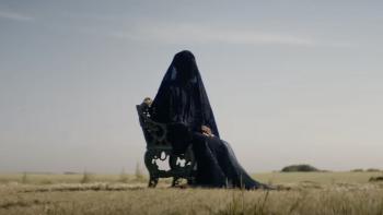 The Woman in the Yard Movie: The woman covered by a black scarf sits in a chair, dried grass at her feet