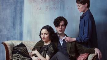 The Laureate: A young White man sits on a sofa with his arm around a woman while another woman places her hand on his shoulder
