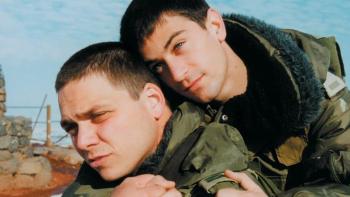 Yossi & Jagger: One male Israeli soldier hugs another from behind, both wearing green army jackets