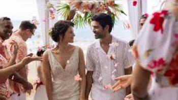You, Always: A smiling couple walks down an aisle at a beach wedding, with guests on either side.