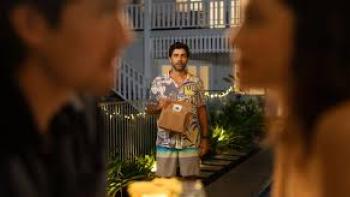 You, Always: Man holding food bag, standing on patio, couple blurred in foreground.