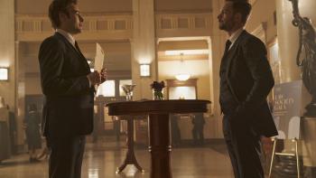 Young Werther movie: Douglas Booth and Patrick J. Adams stand across from each other in a fancy event space hallway, wearing suits