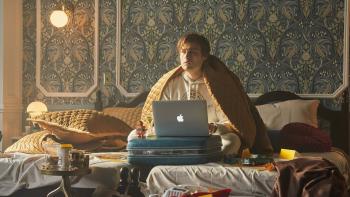 Young Werther movie: Douglas Booth wears a blanket over his shoulders, sitting on a hotel bed with a laptop