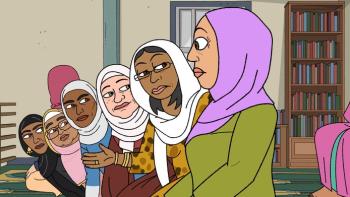 A row of women wearing headscarves lean forward in a row. They stare at a woman at the end, in a green top and pink headscarf.