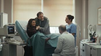A Round of Applause screenshot: A woman is shown in labor in a hospital room surrounded by her husband, doctor and a nurse.