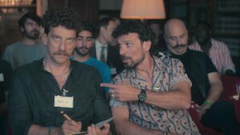 Real Men TV show screenshot: A White man points at another White man who's taking notes in a seminar with more men in the background