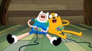 Adventure Time: Side Quests TV show screenshot 1: Jake and Finn sit together on a green floor, each holding game controllers and grinning