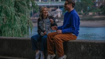 Alice and Steve TV show screenshot 1: Alice and Steve sit on a cement wall next to a river; they are smiling at each other and gesturing broadly