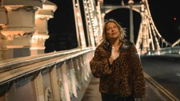 Alice and Steve TV show screenshot 3: Alice walks underneath a lighted bridge wearing a leopard print coat; she smiles up at the sky