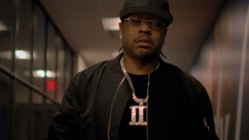 Allen Iv3rson screenshot 2: Older Allen Iverson walking down hall wearing black baseball cap and gold chain with Roman numeral three
