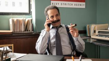 American Classic TV show screenshot 1: Tony Shalhoub sits at a desk while holding a cigar. He wears a button-up shirt, tie and suspenders.