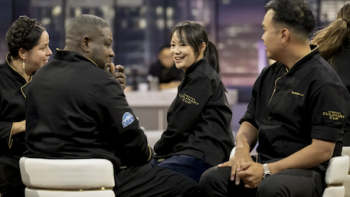 America's Culinary Cup TV show screenshot 3: Contestants in blue chefs coats sit on white chairs around tables. 