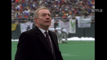 Archival footage photo of Jerry Jones, clad in a suit, standing on a football field in a packed stadium
