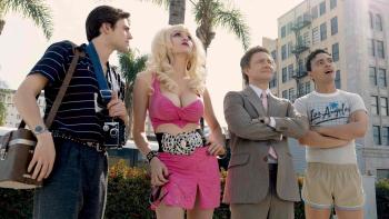A blonde woman clad entirely in hot pink clothing with a low-cut top stands outside with three men, looking skyward.