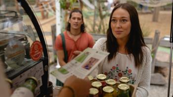 Apple Cider Vinegar TV show screenshot 3: Milla proffers a tray of home-canned liquids as her partner stands behind her. 