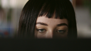 Ashley Madison: Sex, Lies, and Scandal TV show screenshot 3: A woman with dark hair and blue eyes behind a computer screen. 