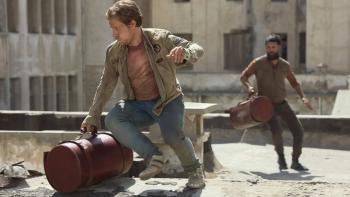 Atomic TV show screenshot 3: Alfie Allen and Shazad Latif run across a building rooftop. They both carry red leather bags shaped like cylinders.