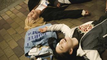 Baby Assassins Everyday!: Mahiro (top) and Chisato (bottom) lie outside on the ground, laughing but tired and injured. They have bruises and bandages.