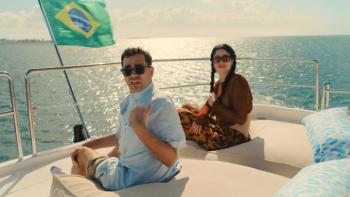 Big Mistakes: Morgan and Nicky sit on a large boat on a waterway; the flag of Brazil flies and Nicky holds a beer; both are looking back with unease