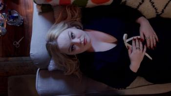 Big Mood TV show screenshot 1: Overhead shot of Maggie, dressed in a low-cut black dress, laying back on her couch with hands clasped across her torso
