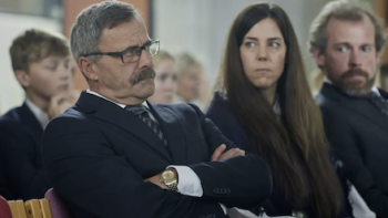 Billionaire Island screenshot 2: Gjert Meyer sits with arms folded in church. 