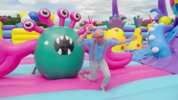 Blippi's Ultimate Bounce House Challenges TV: Blippi running from a green monster with eight pink eyes in a sea-monster themed bounce house.
